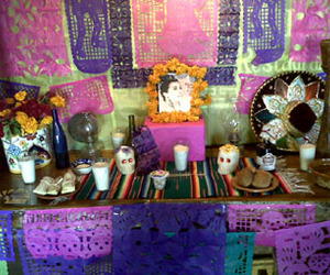 An altar de muertos dedicated to the late singer Lola Beltran, whose CD centers the altar. Plates hold tamales and bread; a bottle of liquor and concert tickets are also seen. © Daniel Wheeler, 2009