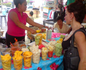 Glasses of sliced mango, jicama, pineapple, cucumber and watermelon are available to take home, or eat on the spot with a squeeze of lime and a sprinkling of salt and chile. In the background, another tianguis merchant sells stylish clothes. © Daniel Wheeler, 2009