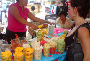 Glasses of sliced mango, jicama, pineapple, cucumber and watermelon are available to take home, or eat on the spot with a squeeze of lime and a sprinkling of salt and chile. In the background, another tianguis merchant sells stylish clothes. © Daniel Wheeler, 2009