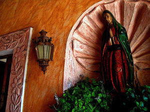 A wonderfully-restored colonial home in San Miguel de Allende is adorned with statuary, candles, and greenery. A sculpture of the Virgin of Guadalupe resides in a shell-adorned niche and graces the main entrance of the home. This original photograph forms part of the Olden Mexico collection. © Darian Day and Michael Fitzpatrick, 2009