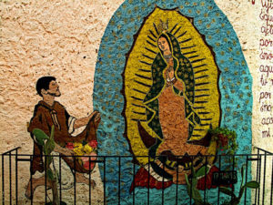 The Virgin of Guadalupe appears to Juan Diego in a life-sized street shrine tucked into a narrow alley in San Miguel. Offerings and decorations on the sidewalk below are protected by a small railing. Nearby are images of Jesus in thorns and the Archangel. This original photograph forms part of the Olden Mexico collection. © Darian Day and Michael Fitzpatrick, 2009