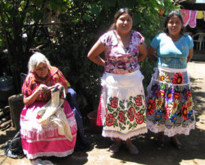 Hermelinda Reyes Ascenio, left, her granddaughter, Elena Reyes Remigio, center, and her grandson Heraclio's wife pose in Elena's Cocucho, Michoacan yard. They show off their bright embroidery work. © Travis Whitehead, 2009