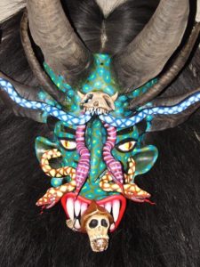 A skull emerges from the toothy mouth of a frightening horned creature, and snakes slither across the face. By mask artisan Prudencio Guzman, this mask is named "The Conscience." It is a Tastoan mask, worn by costumed dancers who battle Saint James each year on July 25th. © Kinich Ramirez, 2006