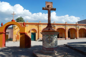 An arched walkway surrounds the courtyard of San Sebastián Mártir Church in Bernal, Querétaro. In the center of the atrium stands a beautiful cross of carved quarry stone. © Jane Ammeson 2009