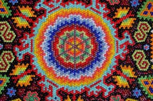 The sacred blue deer, brother of the Huichol people, surround a glowing peyote bud in psychedelic colors. This beadwork art is by Huichol artisan and philosopher Kupihu'ute. © Erin Cassin, 2006