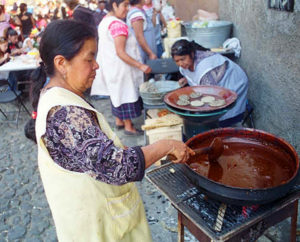 A woman from Paracho prepares mole con pollo in a red clay casserole over a wood fire. Paracho is famous for the fine guitars crafted there.