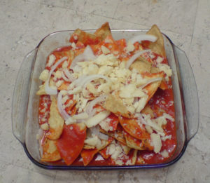 Chilaquiles rojos: fried tortilla chips smothered with a chile-tomato sauce and topped with cheese and onion slices. Heat through in the oven before adding your favorite garnish. © Daniel Wheeler, 2009