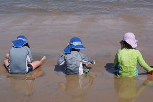 Wide brimmed hats and longe sleeve shirts protect children who play in the sand on a Mexico beach. Cool Pacific waves lap at their feet. © Christina Stobbs, 2011