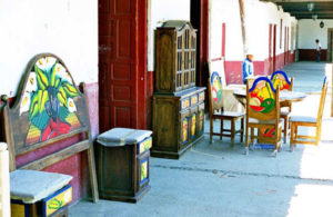 A young maiden with flowers decorates a headboard outside a furniture store on the plaza of Cuanajo. Carved and painted by hand, fruit adorns the dining chairs and table.