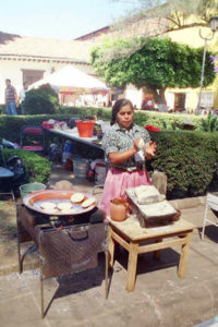 A Purepecha woman participating in the Purepecha Food Show purses her lips in concentration as she slaps dough together for gorditas, one of many dishes served at the event. Corn is ground by hand with a stone mano and metate, then the masa is shaped, as seen here.