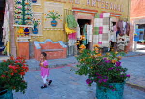 A little girl walks down the main avenue in Bernal, Querétaro. Shops offering a dazzling array of handicrafts frame the child and potted flowers bloom along the sidewalk in this charming pueblo mágico. © Jane Ammeson 2009