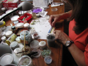 Martha places a bit of peacock feather into the lake to act as a reed. A bit of adhesive wax sits on a jar lid in the foreground.