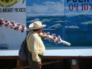 An itinerant mechant carrries a pole festooned with candy apples for sale as he gazes at a mural depicting the sea. San Blass on the Nayarit coast of Mexico is a quiet beach town with a long history. © Christina Stobbs, 2009