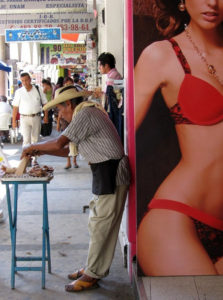 In a stark contrast between old and new, a traditional street food vendor in Acapulco prepares his wares in the shadow of a modern advertising image. © Gerry Soroka, 2009