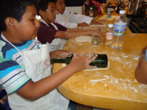 Young students at Chef Pilar Cabrera's Casa de los Sabores cooking school in Oaxaca roll out pizza dough with bottles as rolling pins. © Alvin Starkman, 2011
