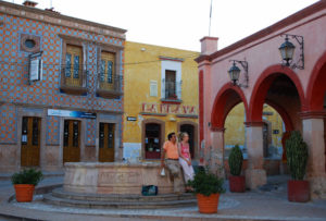 A couple rests beside a fountain to enjoy the scenery in a Bernal, Querétaro plaza. Moorish or Mudejar influence is evident in the decorative ceramic tiles that cover the façade of Casa Tsaya behind them. © Jane Ammeson 2009