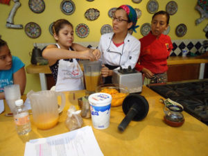 Lead instructor at Chef Pilar Cabrera's Casa de los Sabores Oaxaca cooking school, Ninfa Raigosashows children how to assemble a fruit smoothie with mangos. © Alvin Starkman, 2011