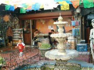 Men working shirtless at heavy duty leather sewing machines behind an unexpected delightful fountain among the souvenirs.