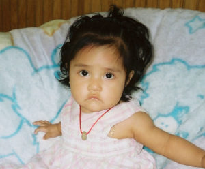 Little Yoana Raquel Cuautle wears an ojo de venado (deer eye) seed to protect her from "mal de ojo." Usually occurring in babies, this is caused by an excess of admiration and the failure to pick up or touch the baby. Interestingly she also wears religious medallion under her dress. © John G. Gladstein, 2010