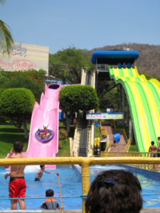 Friends in an inner tube race down a slippery pink water slide. The taller slide to the right features six lanes for individual adventurers to enjoy on a hot day in Mexico. These are part of El Rollo Parque Acuático near Cuernavaca, Morelos. © Julia Taylor, 2008