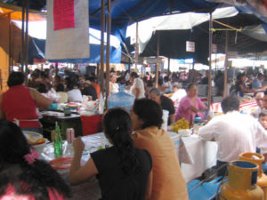 Shaded by tarps, the food market fills up on Sundays. A hand-written menu on hot pink paper hangs overhead. © Julia Taylor 2007