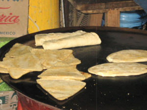 In Tepoztlan's food market, tasty quesadillas (back), itacates (triangles), and tlacoyos (ovals) cook on a comal. © Julia Taylor 2007