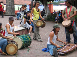 A group of young people drum together in the zocalo. A djembe drum hangs from a red cord around the drummer's neck. Bougarabou drums (named for the sound they make) and a xylophone -- which originated in West Africa and came to Mexico via the Caribbean -- complete the ensemble. © Julia Taylor 2007