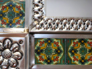 Close-up of a handcrafted wall mirror reveals the intricate tin repoussé, accented by holes punched into the frame. The ceramic tiles are crafted in the style of Mexico's traditional Talavera pottery. © Julia Taylor, 2008