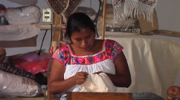 A member of the cooperative in colorful traditional dress embroiders linens by hand.