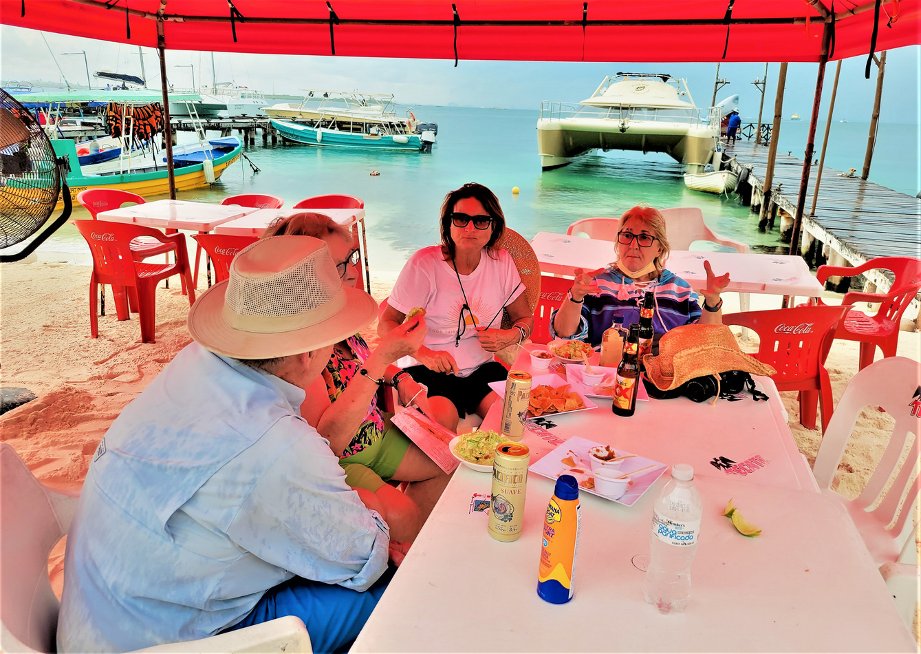 People at table by boats: Island visitors indulging in grilled fresh fish, house made tortillas, and, of course, lobster at the Miramar Lobster House. You can even get your photo taken there and pasted on a bottle to tequila to take home as a souvenir.© 2021 Jane Simon Ammeson