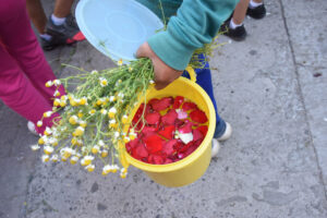 A person carrying a bunch of chamomile and a bucket filled with holy water.© Joseph Sorrentino, 2023